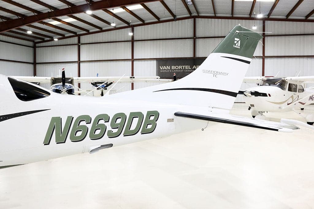 Close-up view of the tail and rear fuselage of a white and green Cessna Stationair TC, registration N669DB, inside a hangar.