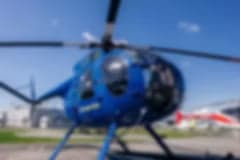 A blue helicopter flying over a snowy mountain range.
