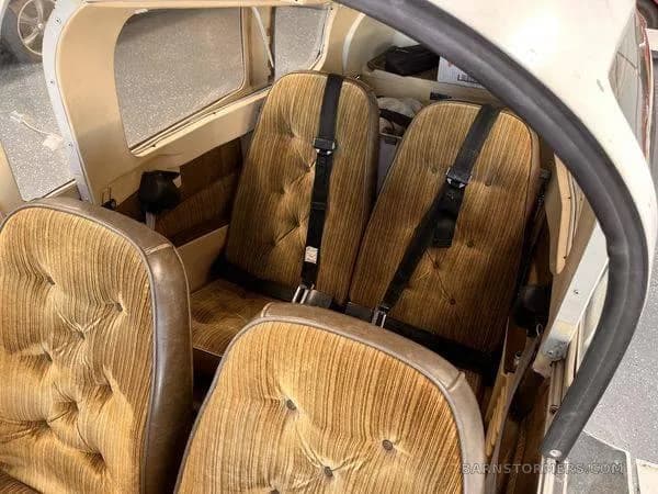 The rear interior of a small aircraft, showing two tan upholstered seats with seatbelts.