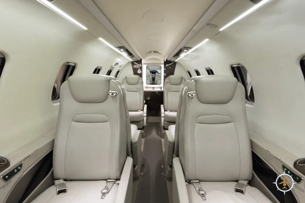 A view down the aisle of the aircraft cabin, showing rows of light-colored leather seats.