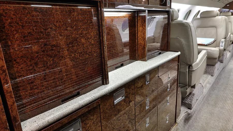 Detailed view of the polished wood cabinetry and light-colored countertop inside a business jet cabin.