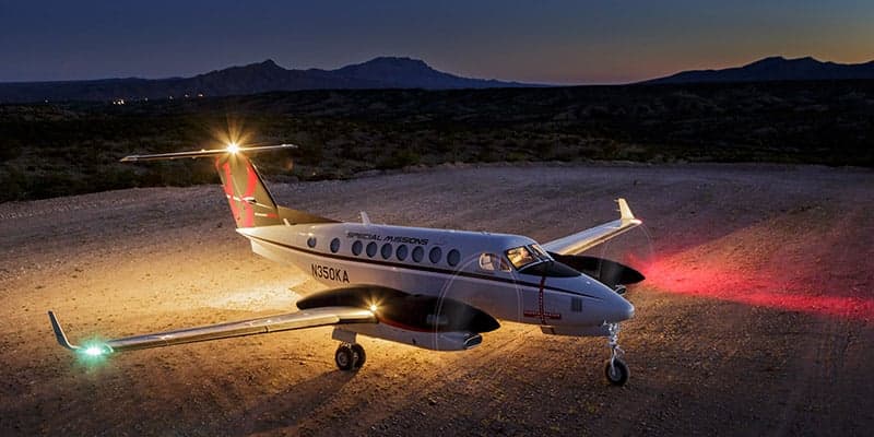 King Air 350 parked on a dirt field at dusk with lights on.