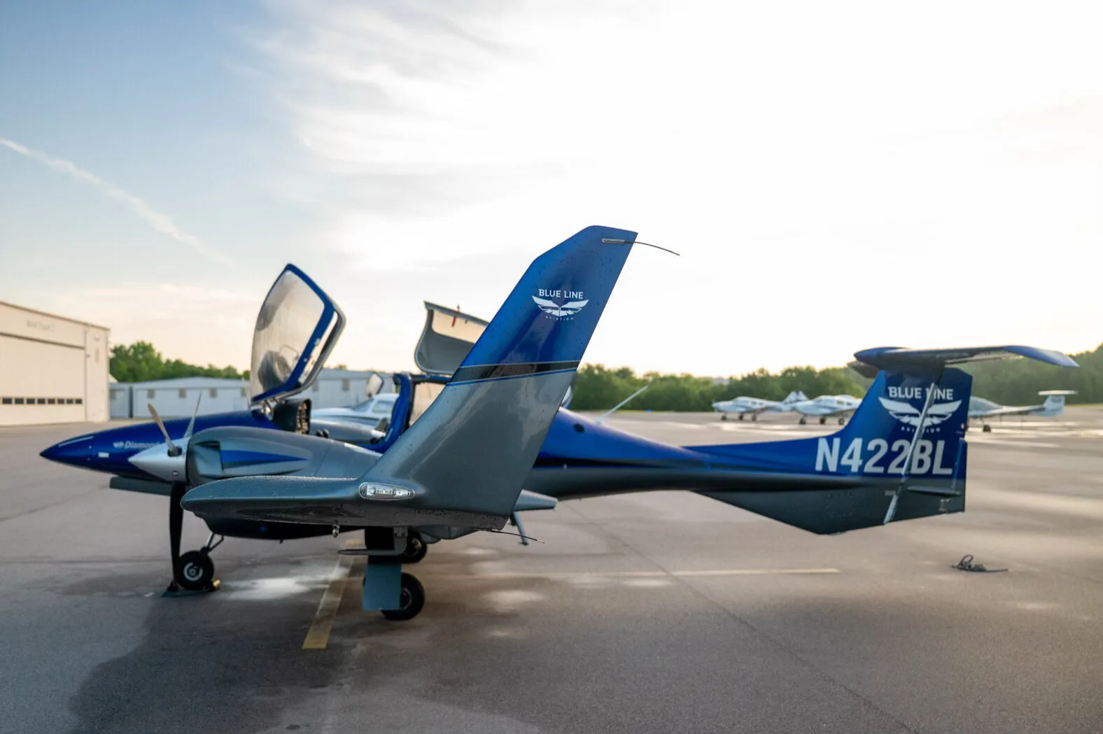 Side view of the blue and grey Diamond DA42NG aircraft, N422BL, with its canopy open on an airfield.