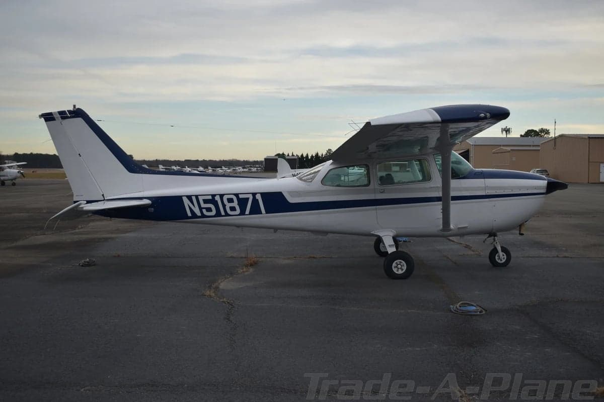 A white Cessna 172 with blue and grey stripes (N51871) is parked on a tarmac, viewed from the left side.