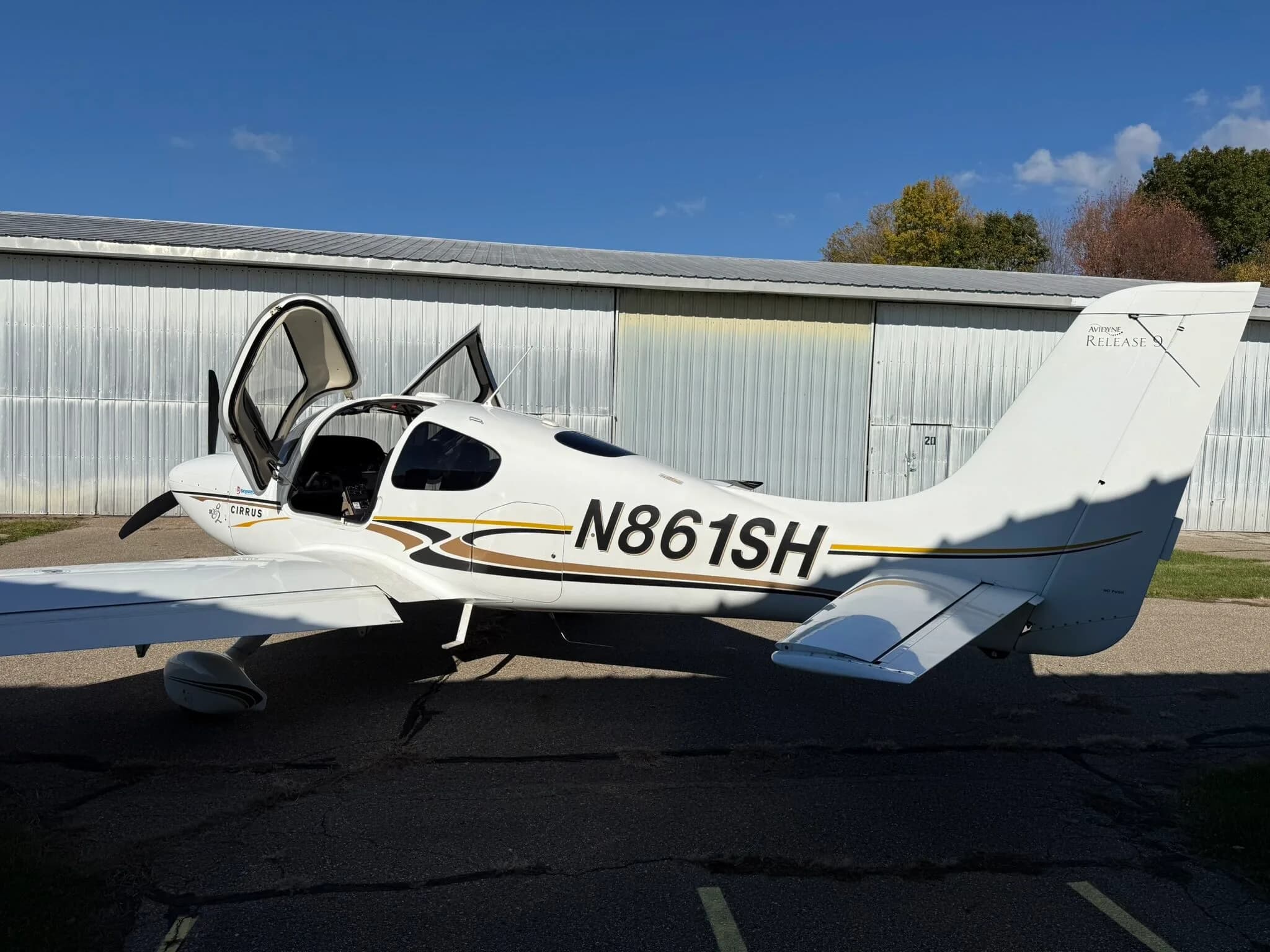 A side view of a white Cirrus SR20 aircraft, registration N861SH, with its doors open, parked on an asphalt ramp.