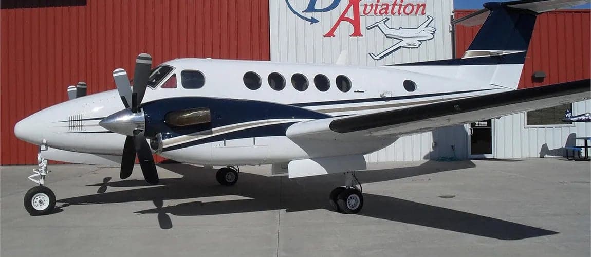 A King Air aircraft is parked in front of a hangar with the company logo.