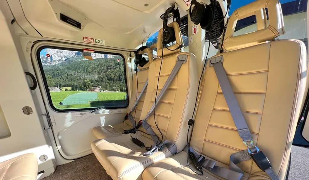 The helicopter's interior cabin features beige seats and a view of mountains through the window.
