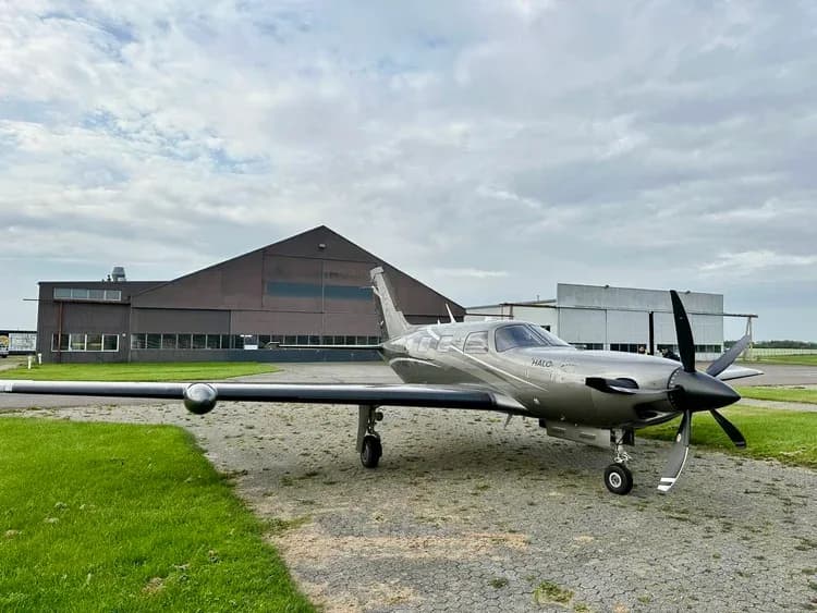 A Piper M600 HALO aircraft parked on the tarmac in front of a hangar on a cloudy day.