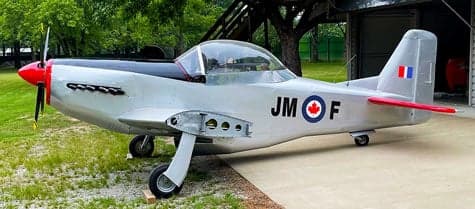 A silver and red aircraft with Canadian markings is parked outside a hangar.