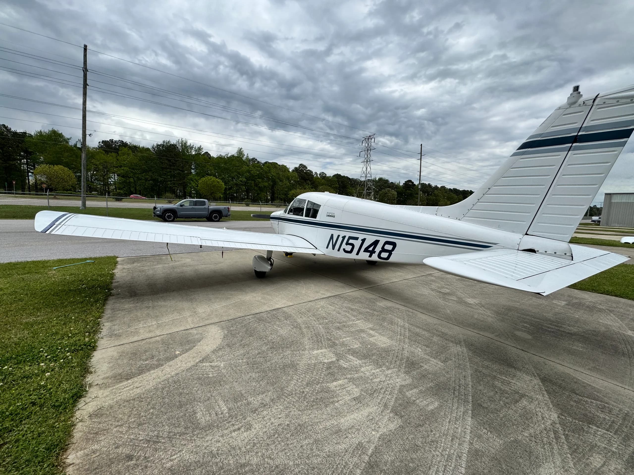 Three-quarter rear view of a white single-engine aircraft, N15148, with dark blue stripes, parked on concrete.