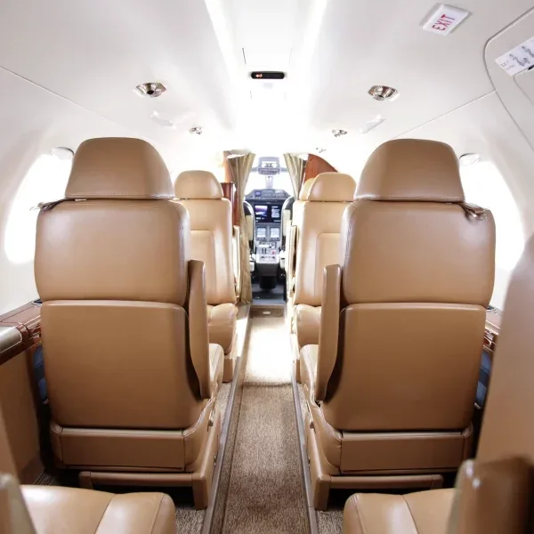 A private jet cabin interior with tan leather seats looking forward towards the cockpit.