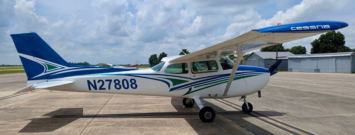 A Cessna 172 Skyhawk with a blue and white paint scheme is parked on the tarmac.