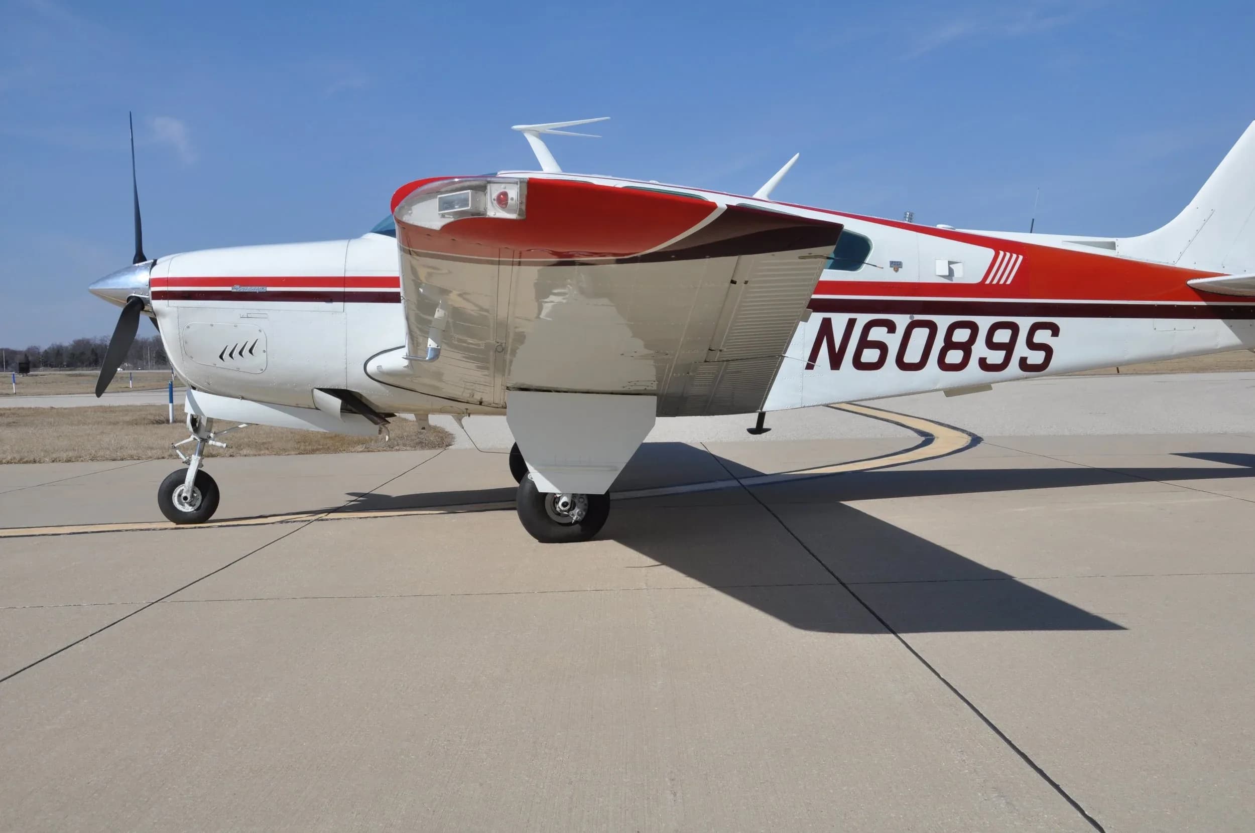 A close-up side view of the white aircraft N6089S, highlighting the wing and fuselage with red and brown stripes.