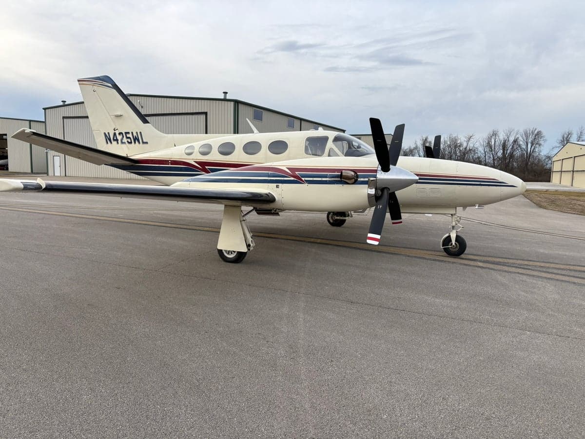 Side view of a white twin-engine propeller aircraft with dark red and blue stripes, tail number N425WL, parked on an airport tarmac.