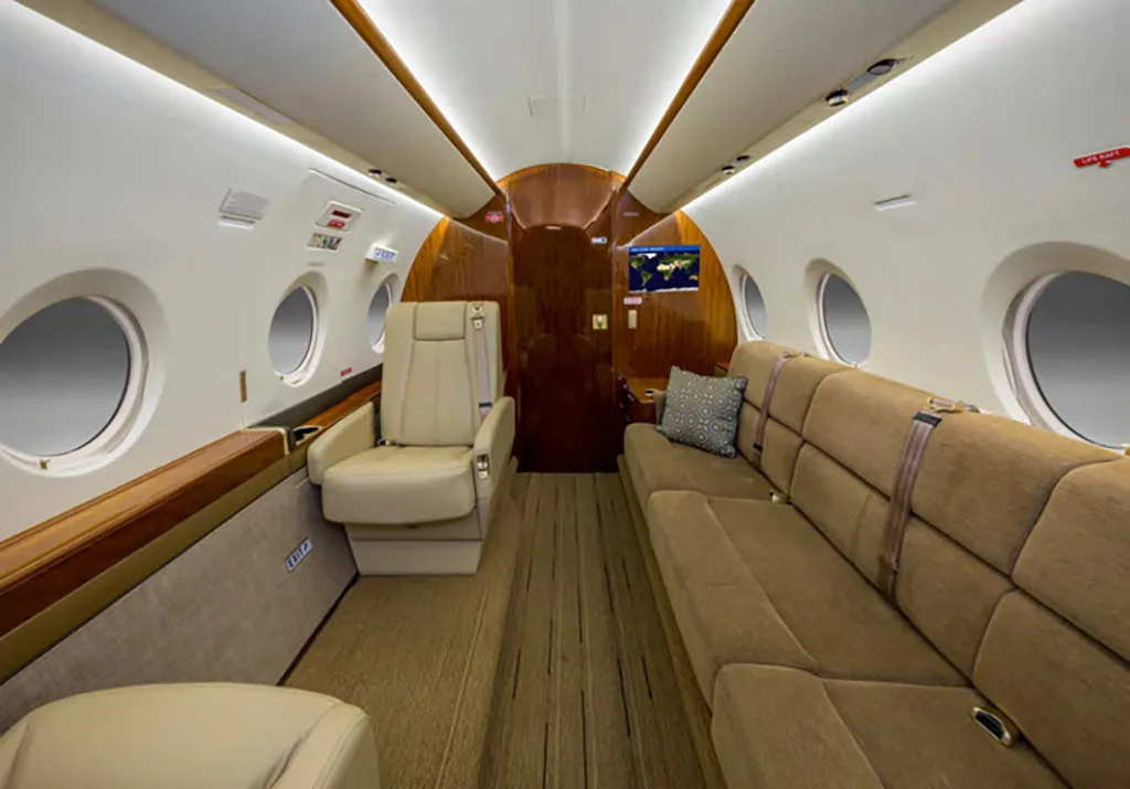 The aircraft's interior cabin features a long brown sofa and a single beige seat with wood paneling.