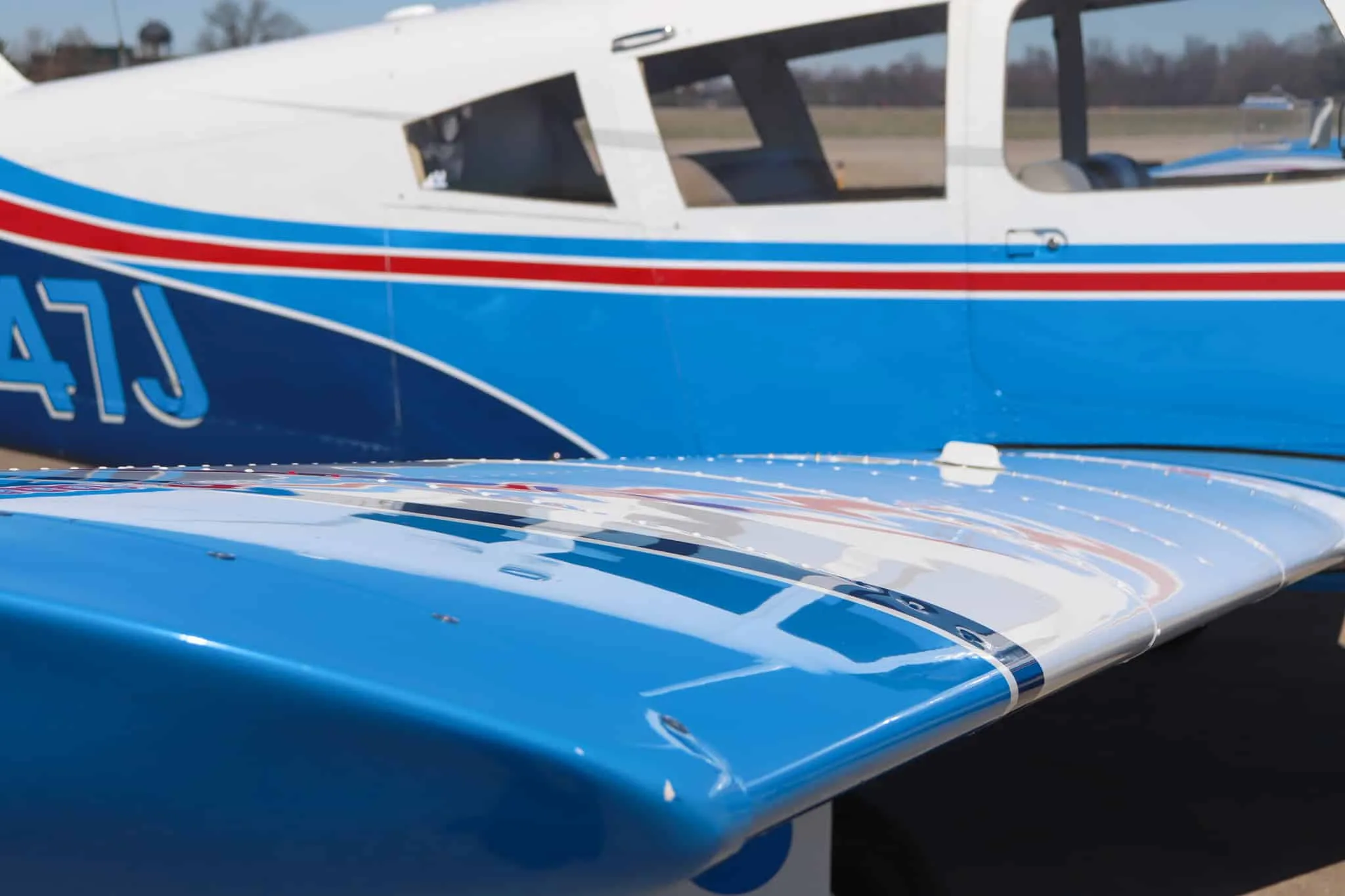 A close-up of the wing and fuselage of the blue and white Piper Cherokee aircraft, showing the N-number.