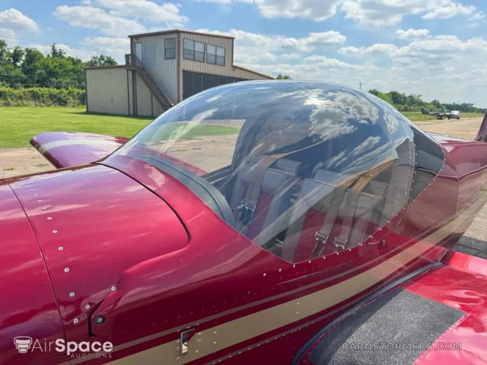 A close-up side view of the red Vans RV-6 aircraft's clear bubble canopy and fuselage, parked on an airfield.