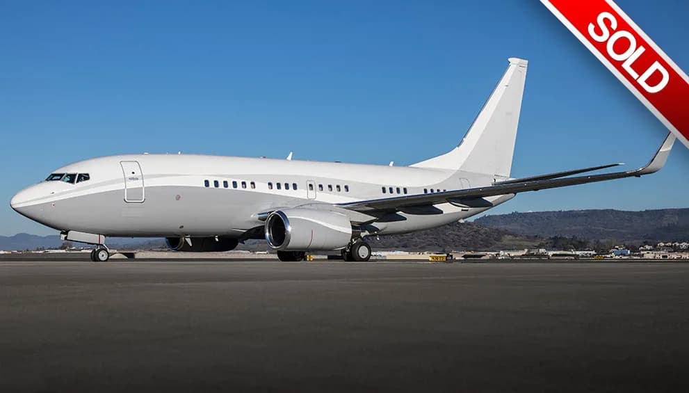 A Boeing 737 in a two-tone grey and white paint scheme sits on an airport tarmac under a clear blue sky.