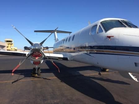 A King Air aircraft is parked on the tarmac with propeller covers installed.