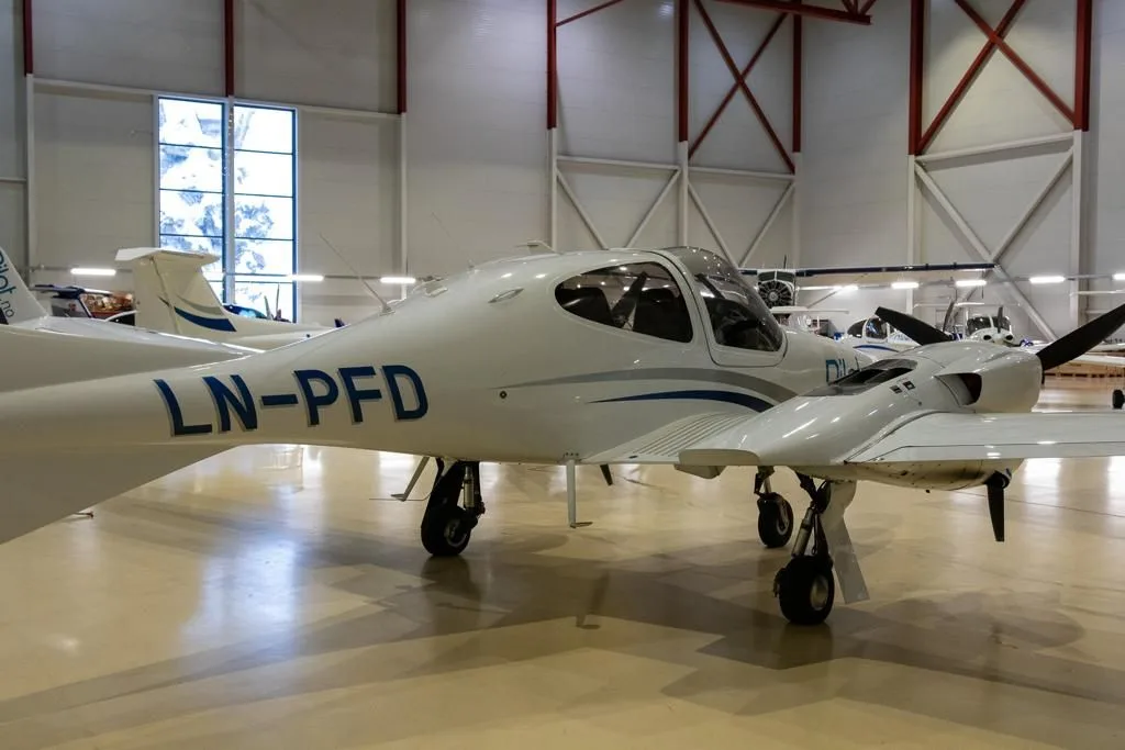 A white Diamond DA42 aircraft with blue and grey stripes and "LN-PFD" registration in a hangar.