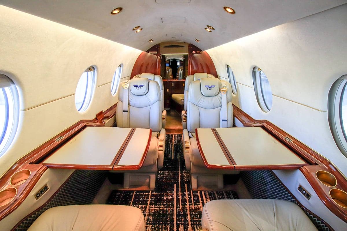 View of the Beechjet 400A cabin with tan leather seats, wood trim, and tables extended.