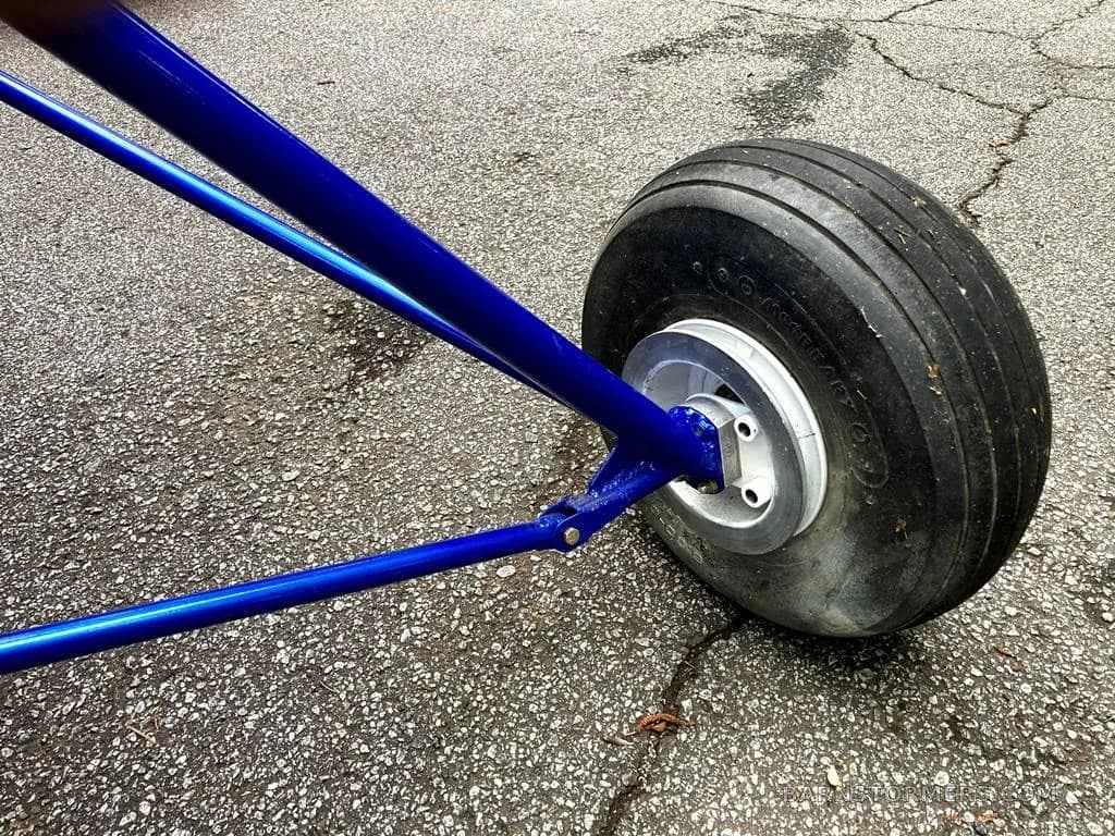 A close-up of the rear landing gear and wheel of the blue ultralight aircraft frame on asphalt.