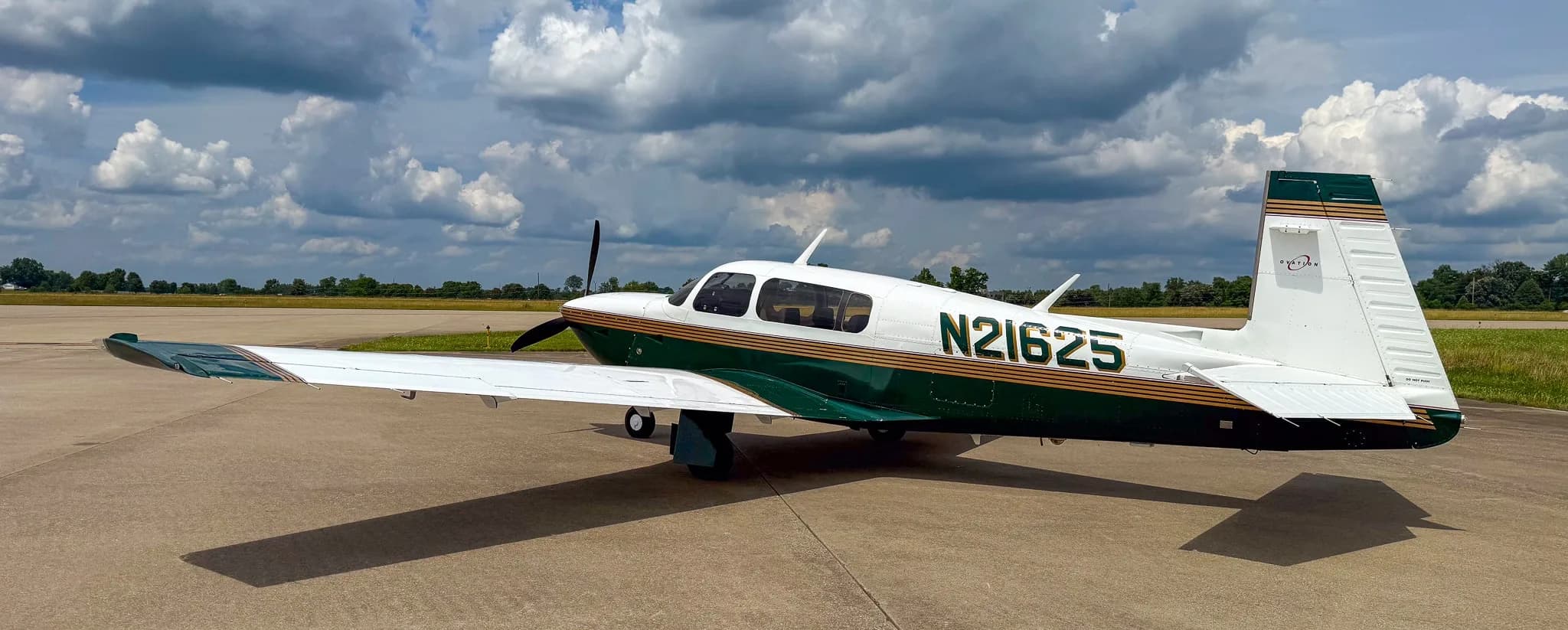 A side view of the white and green Mooney M20 aircraft with registration N21625 on an airfield.