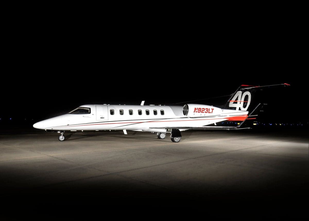 A Learjet 40 with a white and red paint scheme parked on a tarmac at night.