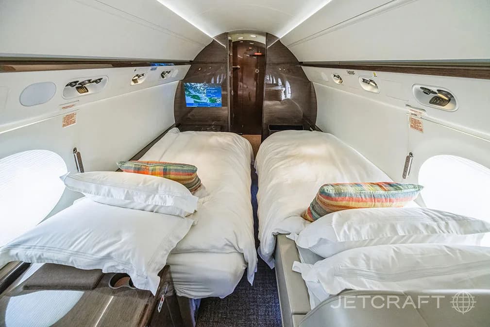 Two beds made up with white linens and colorful pillows inside a private jet cabin.
