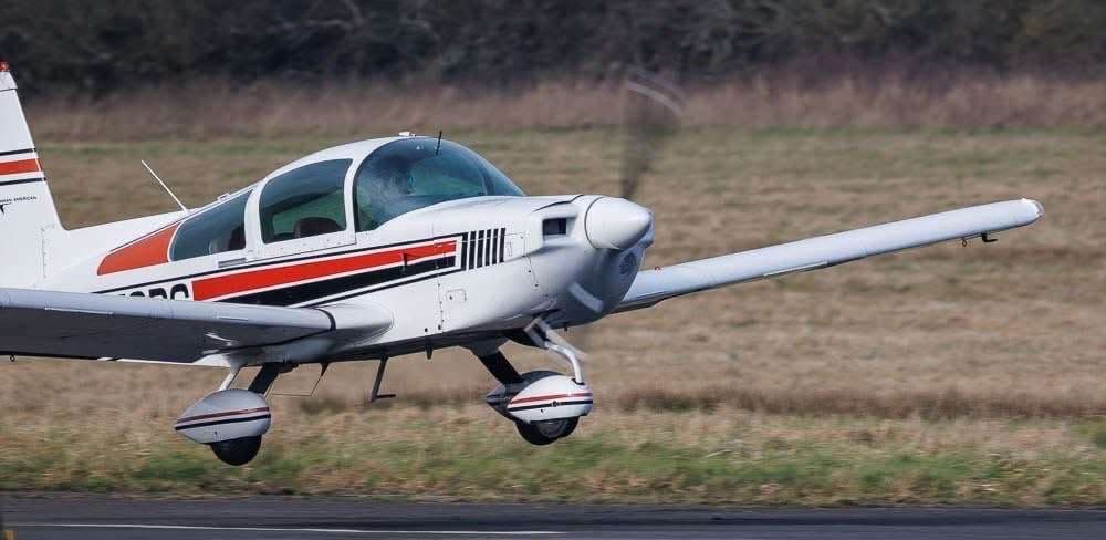 A Mooney M20C aircraft taking off from a grassy runway.