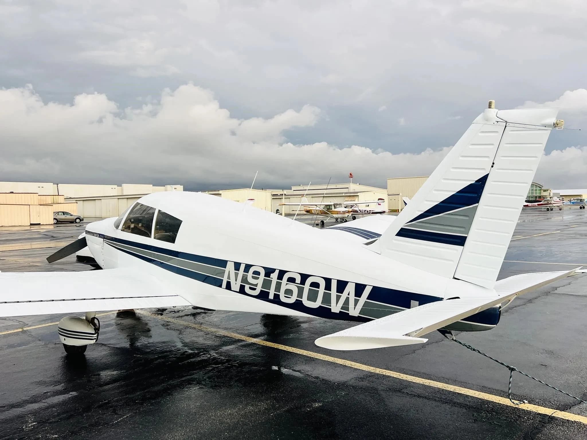 Rear-side view of a white Piper Cherokee 235 B (N9160W) parked on a wet tarmac.