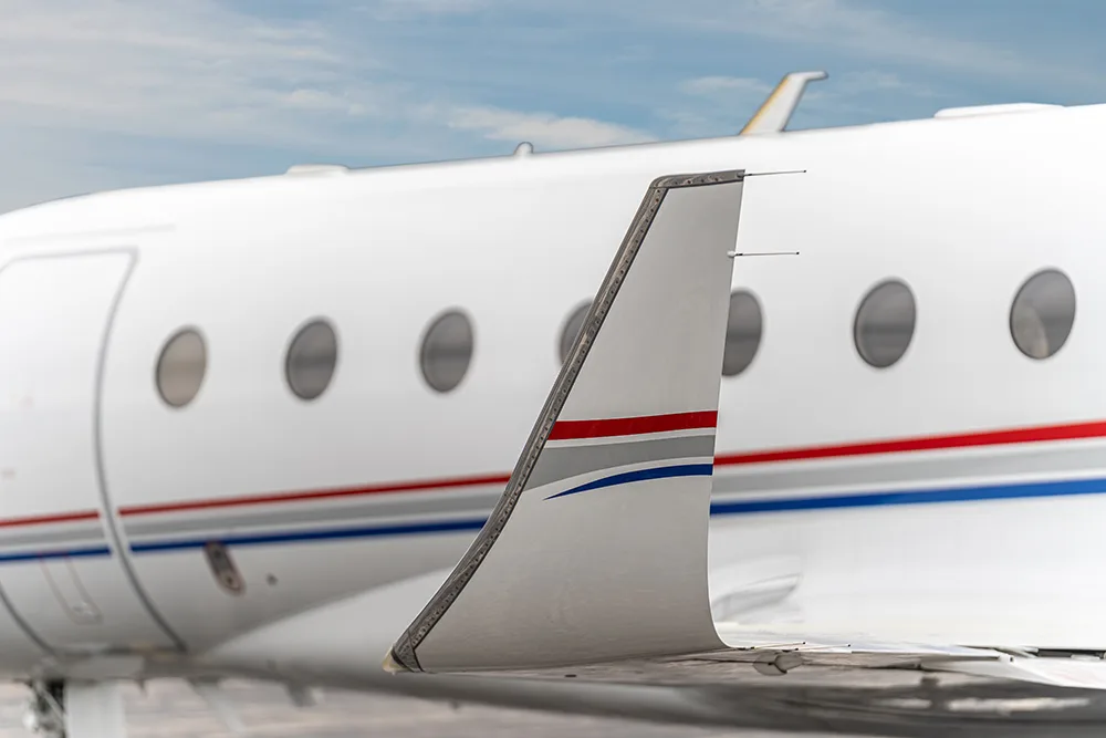 A close-up of the winglet and fuselage of a white business jet, featuring red and blue accent stripes.