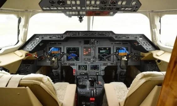 The cockpit of a business jet with multiple digital displays and beige leather seats.