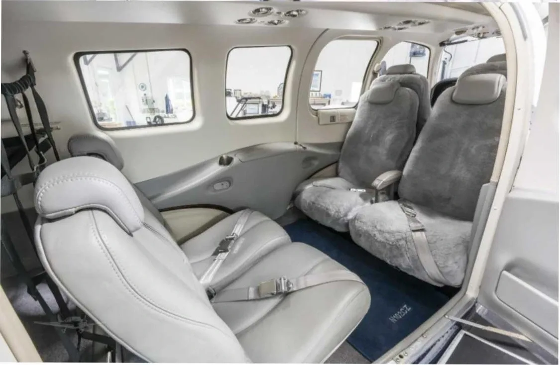 The interior cabin of a small aircraft with gray leather seats and two sheepskin-covered seats.