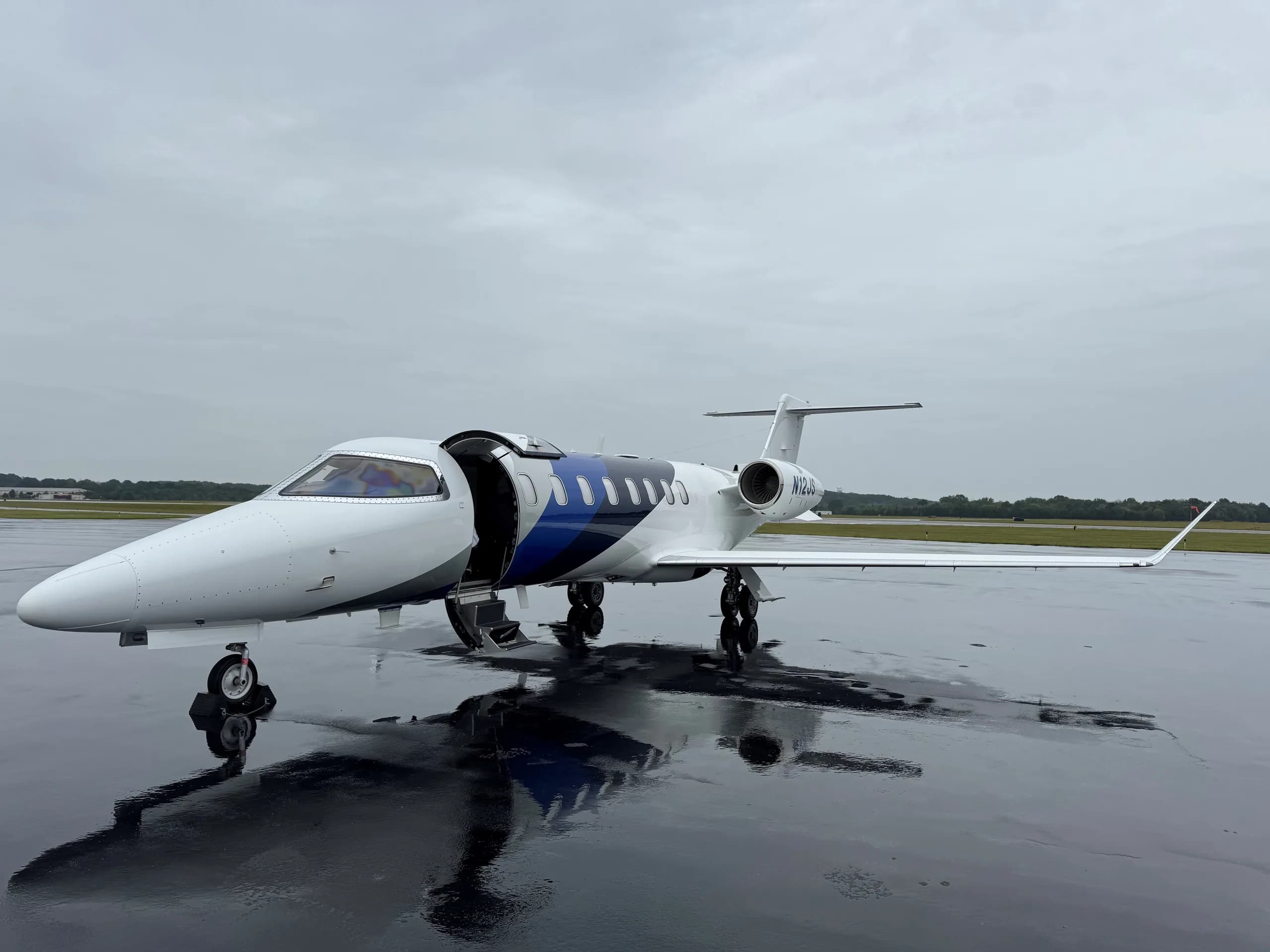 A white and blue jet is parked on the tarmac with the door open.