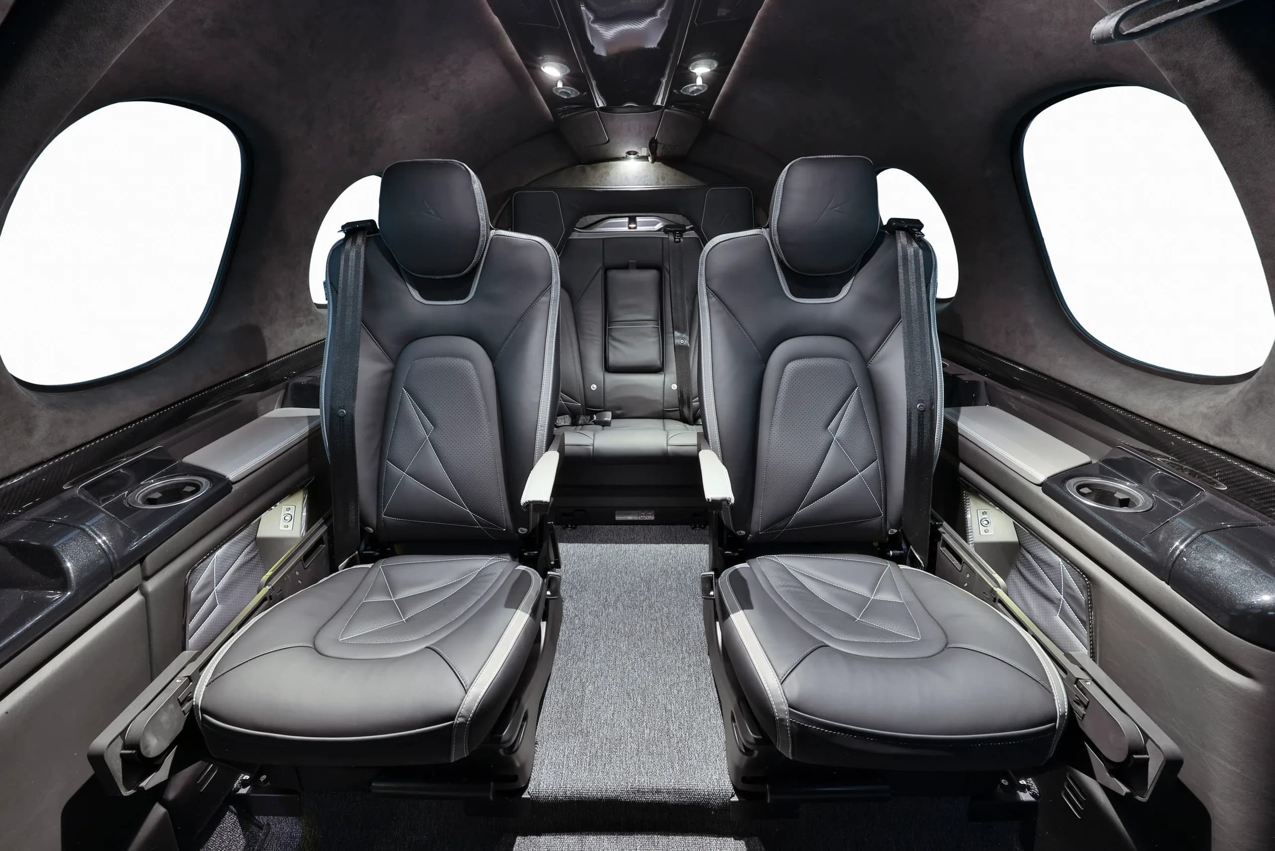 The interior cabin of a private jet features black leather seats with white stitching.
