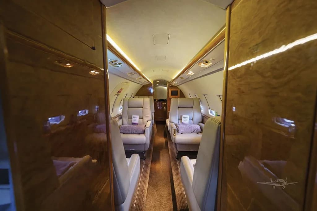 A perspective view of the Dassault Falcon 50's cabin, showcasing the beige leather seating arrangement and polished wood bulkheads.