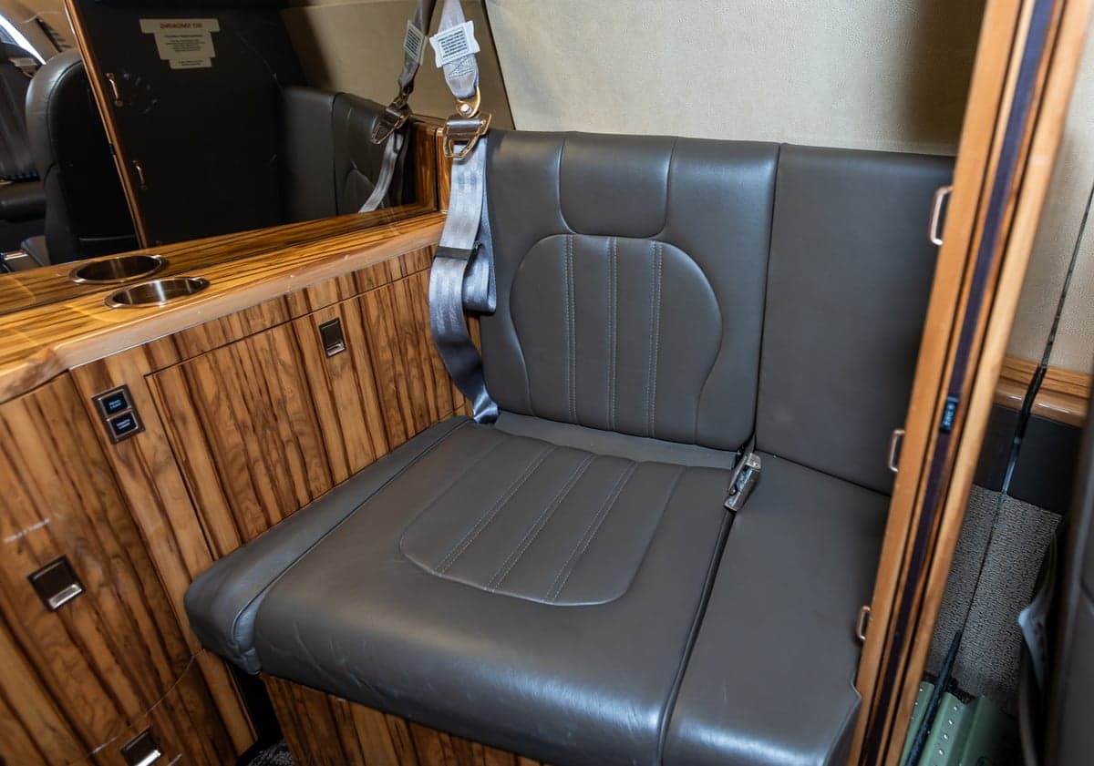 A single leather seat with a seatbelt is shown inside the aircraft cabin.