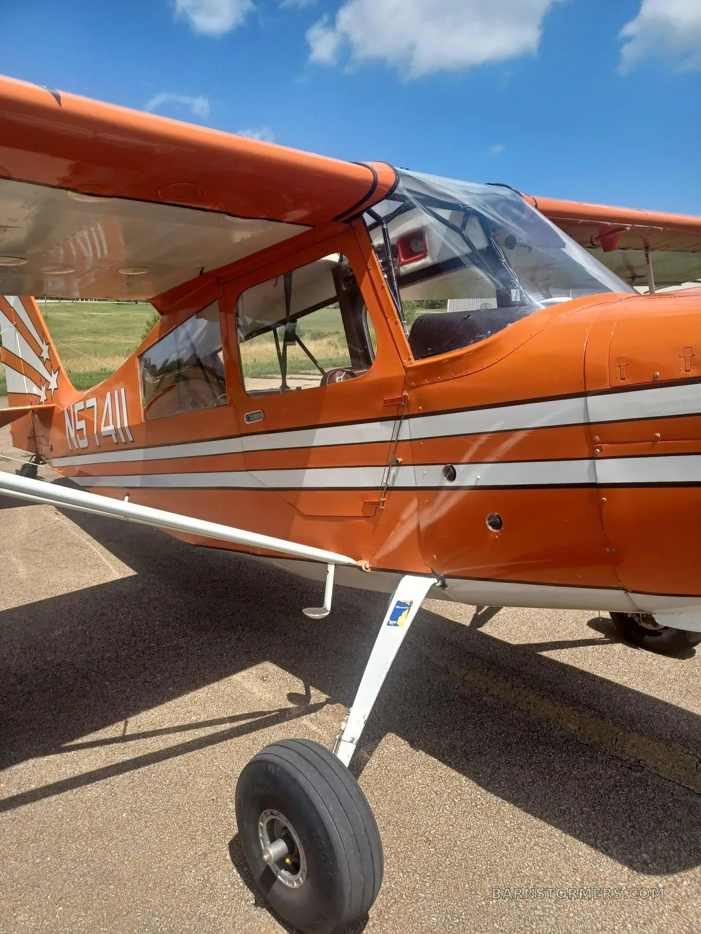 A close-up side view of the orange and white aircraft's cockpit and front landing gear, showing registration N57411.