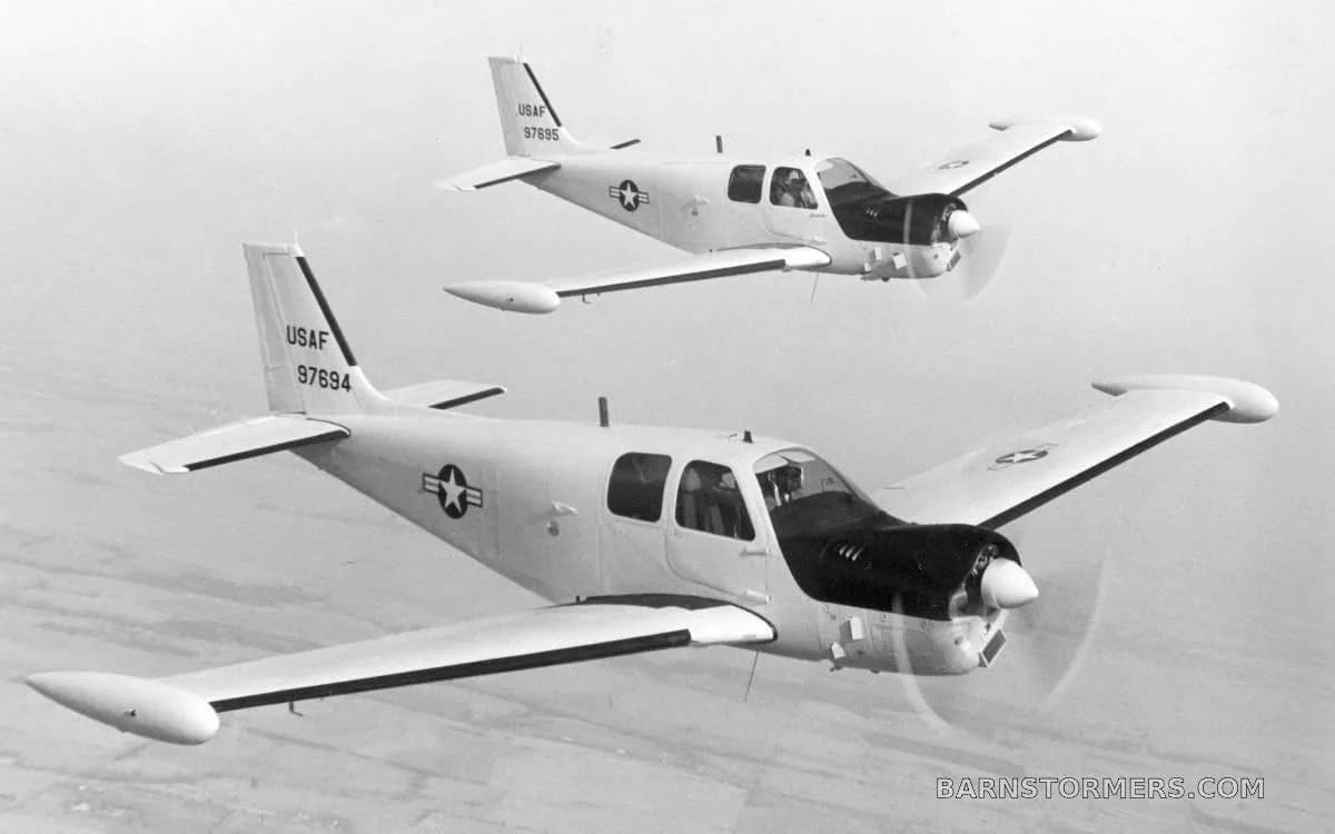 Two USAF Beechcraft T-34 Mentor aircraft fly in formation against a cloudy sky in a black and white photo.