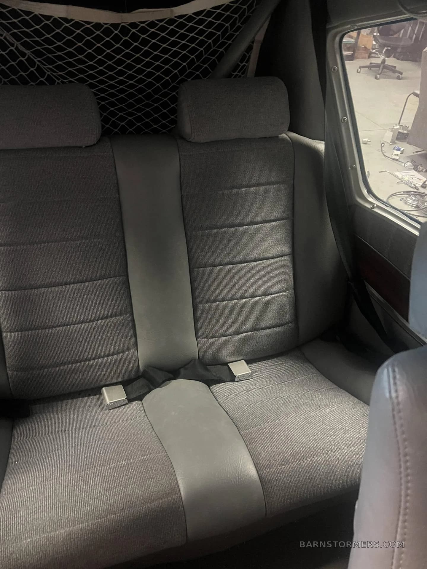 The gray and fabric rear seats of an aircraft interior with a cargo net behind them.