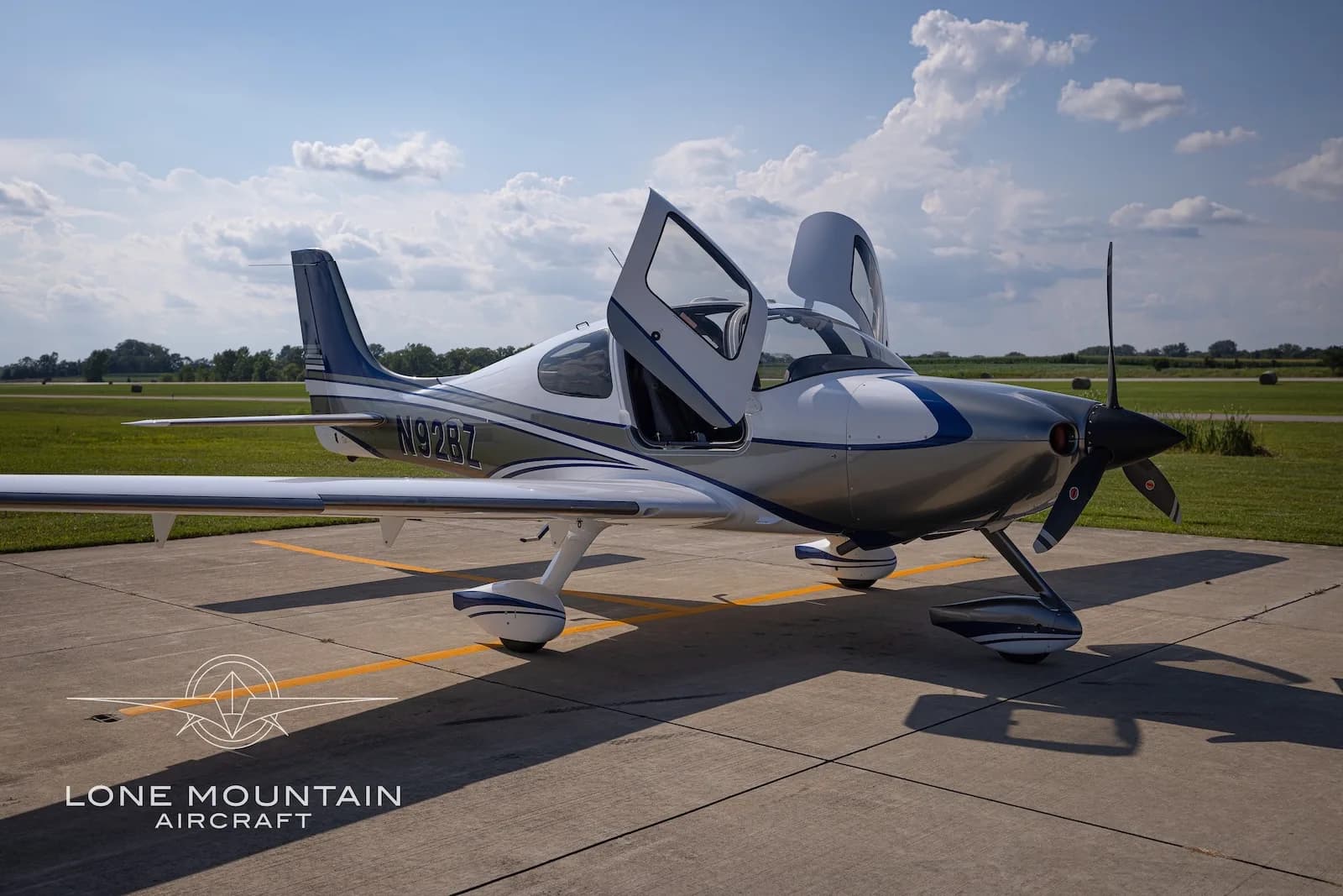 A white and silver Cirrus SR22 aircraft with blue accents, registration N92BZ, parked on an airfield with its doors open.
