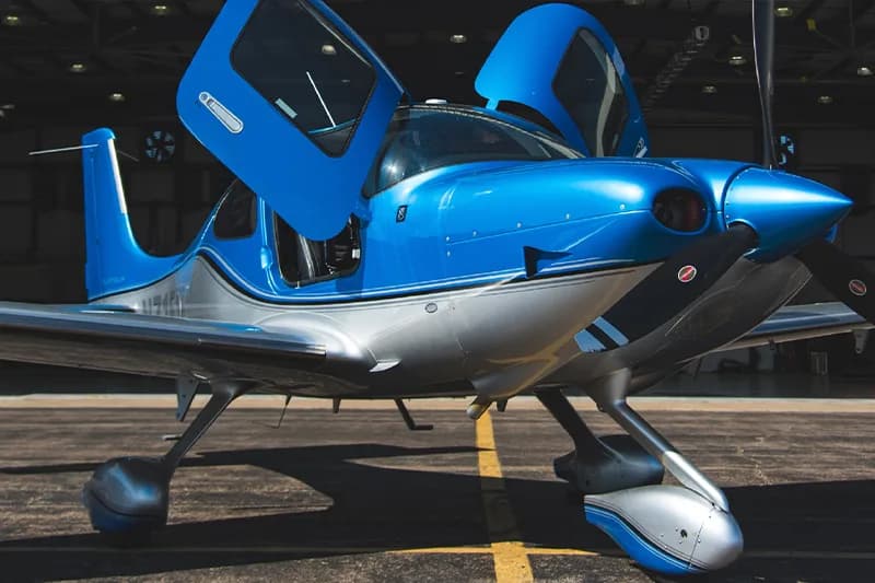 A blue and silver Cirrus aircraft with its doors open.