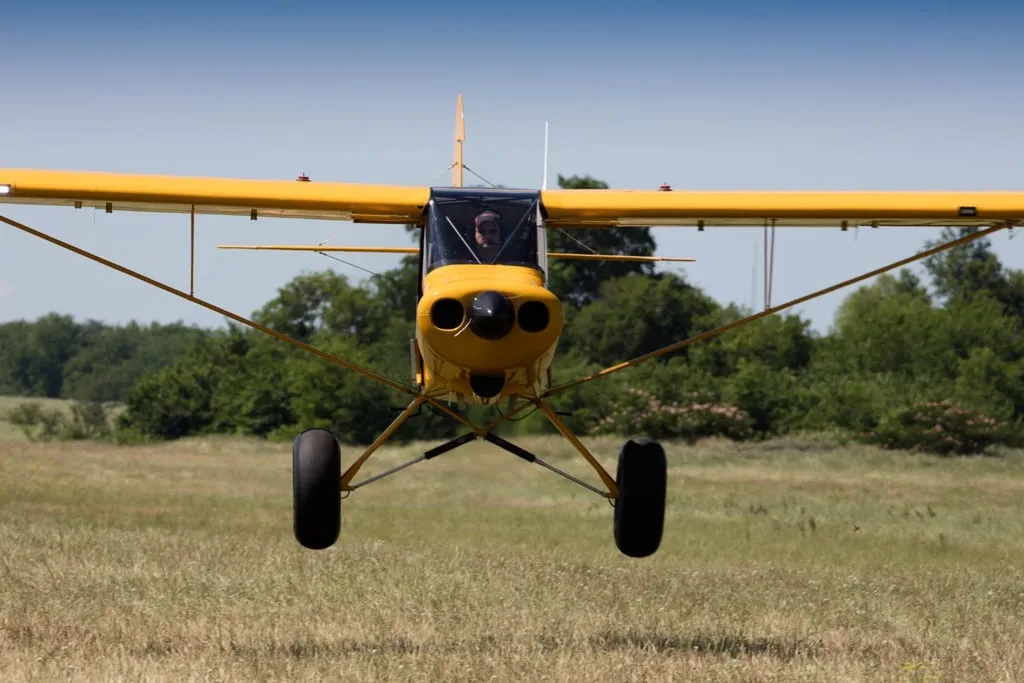 Yellow aircraft landing on a grassy field.