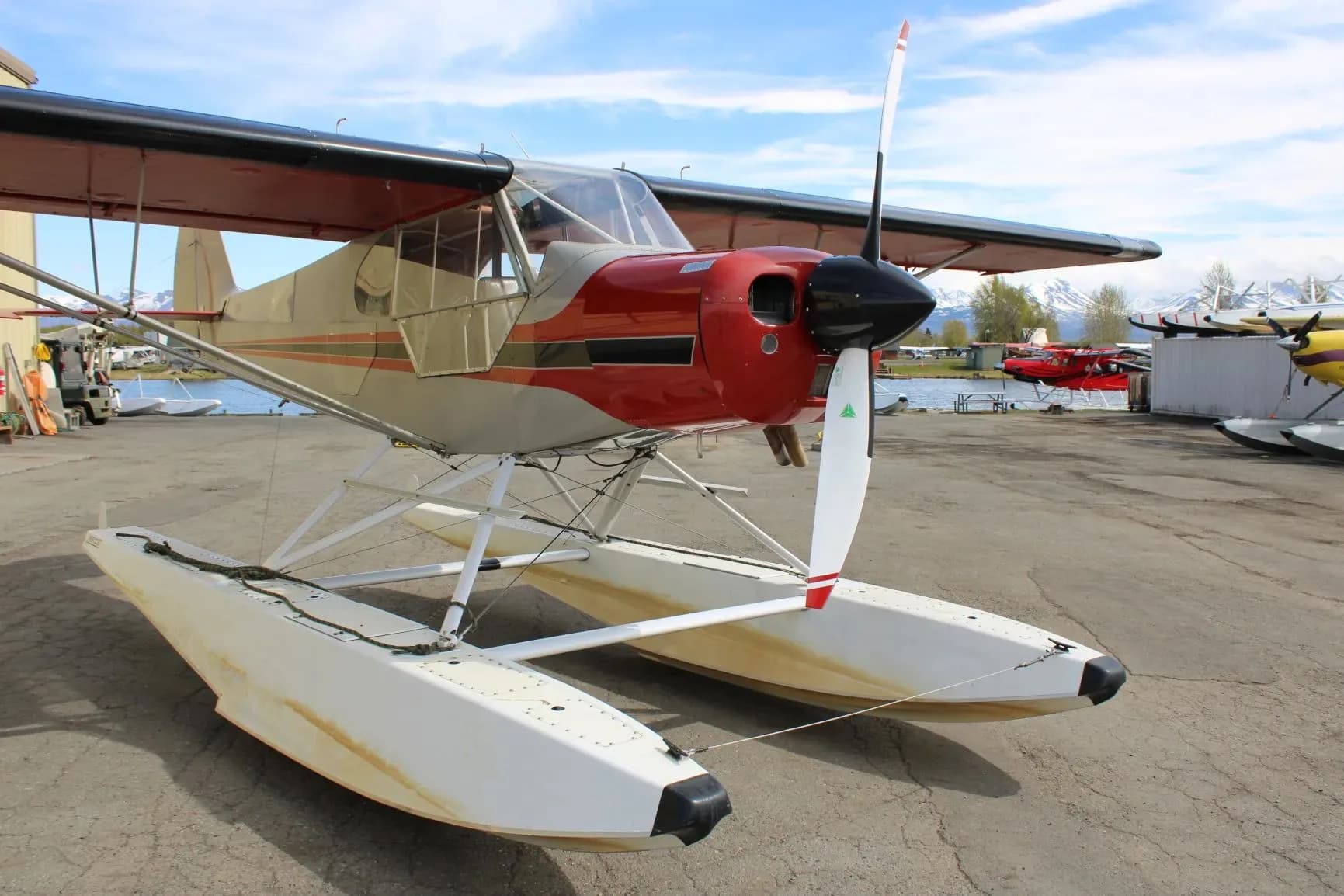 A close-up front-side view of the red and grey floatplane's nose, propeller, and floats.