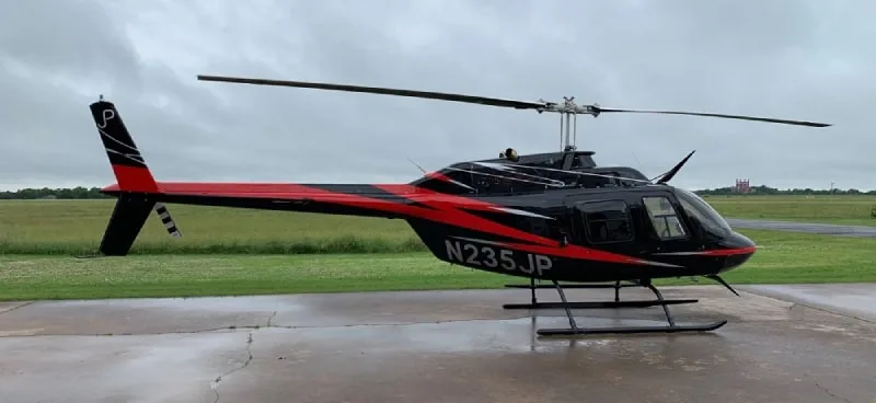 Bell 206L-4 helicopter, registration N235JP, parked on a concrete pad with a black and red paint scheme.