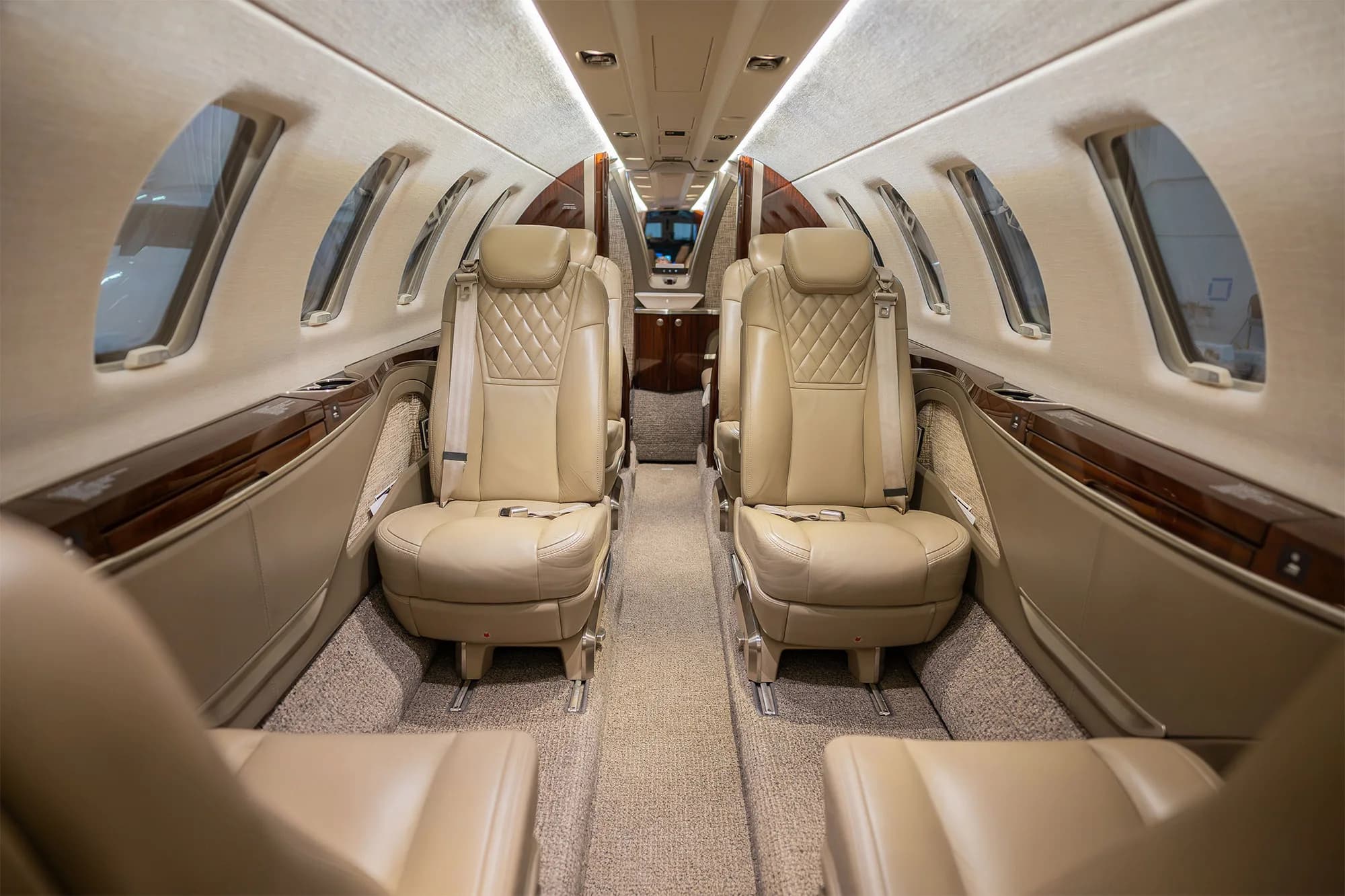 The elegant interior cabin of a business jet with beige quilted leather seats and wood paneling.