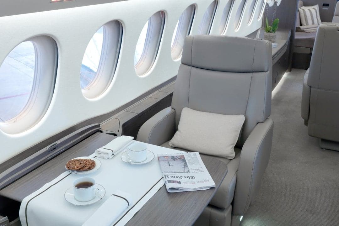 Interior of the aircraft featuring a gray leather seat, a table with tea and cookies, and a newspaper.