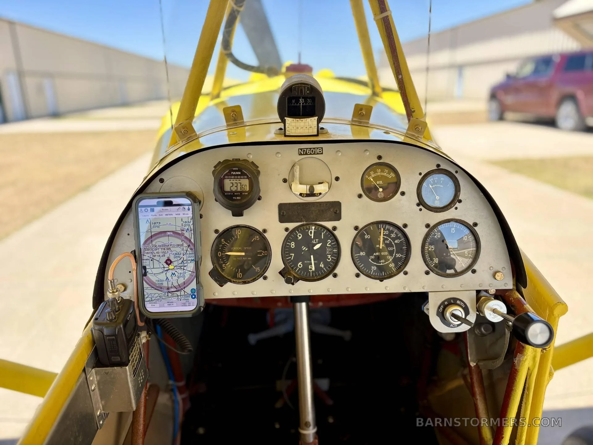The instrument panel of a yellow biplane, featuring various gauges and a mounted smartphone displaying a map.