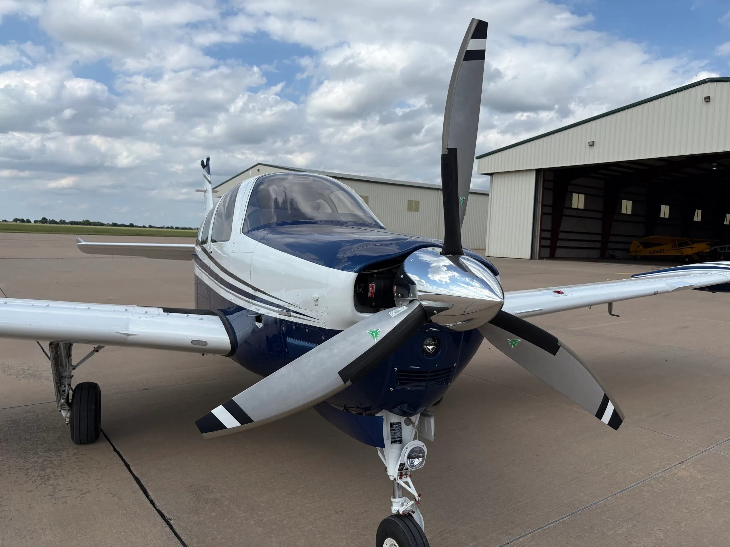 A close-up front view of the white and blue Beechcraft Bonanza N686AG, showing its propeller and open engine cowling.